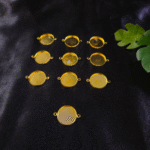 “Gold double-sided round resin bezels arranged on a black fabric background with green leaves