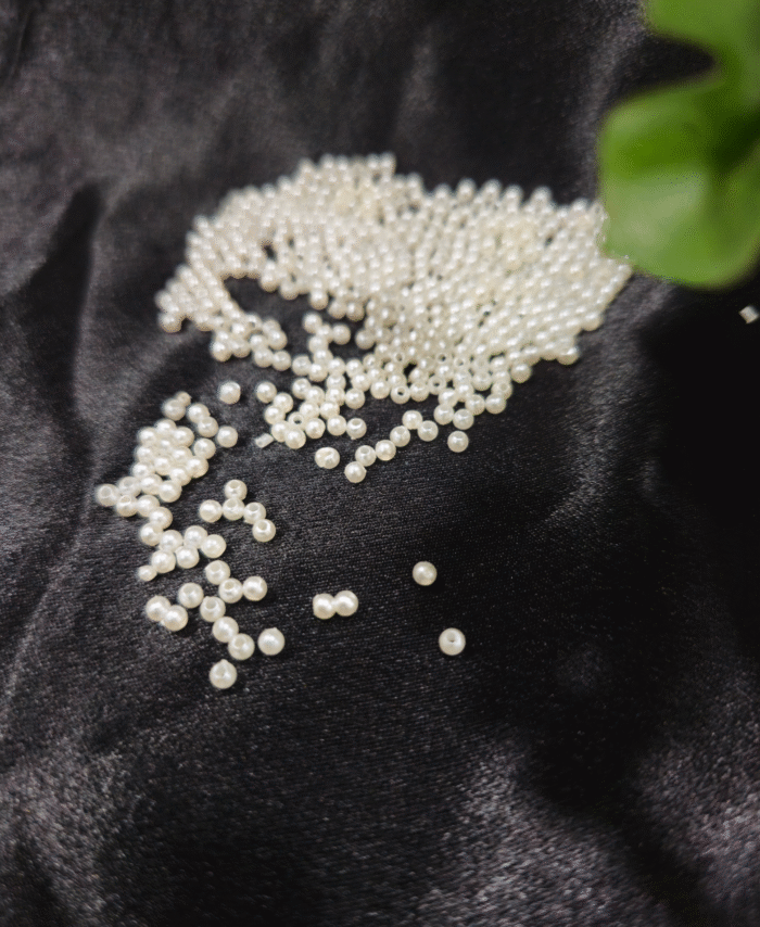 Ivory round pearl beads scattered on black fabric for jewellery making and craft use"