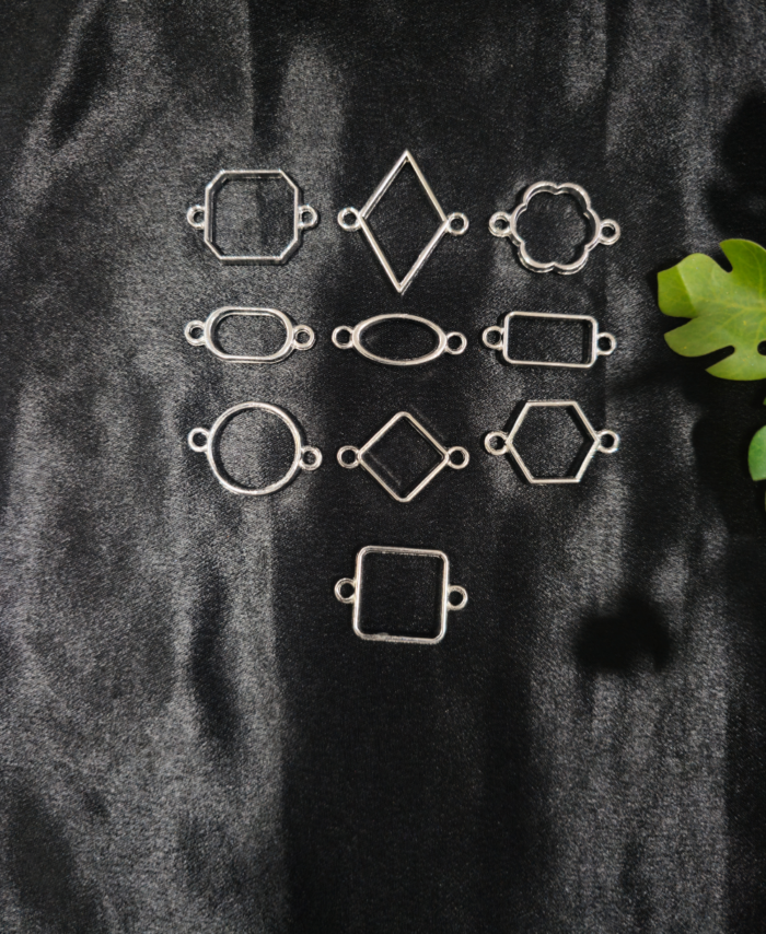 Silver-plated assorted resin bezels in multiple shapes are displayed on a black background. Mixed-shape silver bezels with double hooks arranged neatly for resin jewellery making.