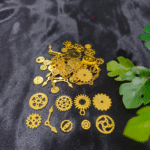 Golden steampunk gears and clock parts scattered on a black background for resin craft use. Various gold metal gears, cogs, and clock hands are displayed for DIY resin jewellery making.