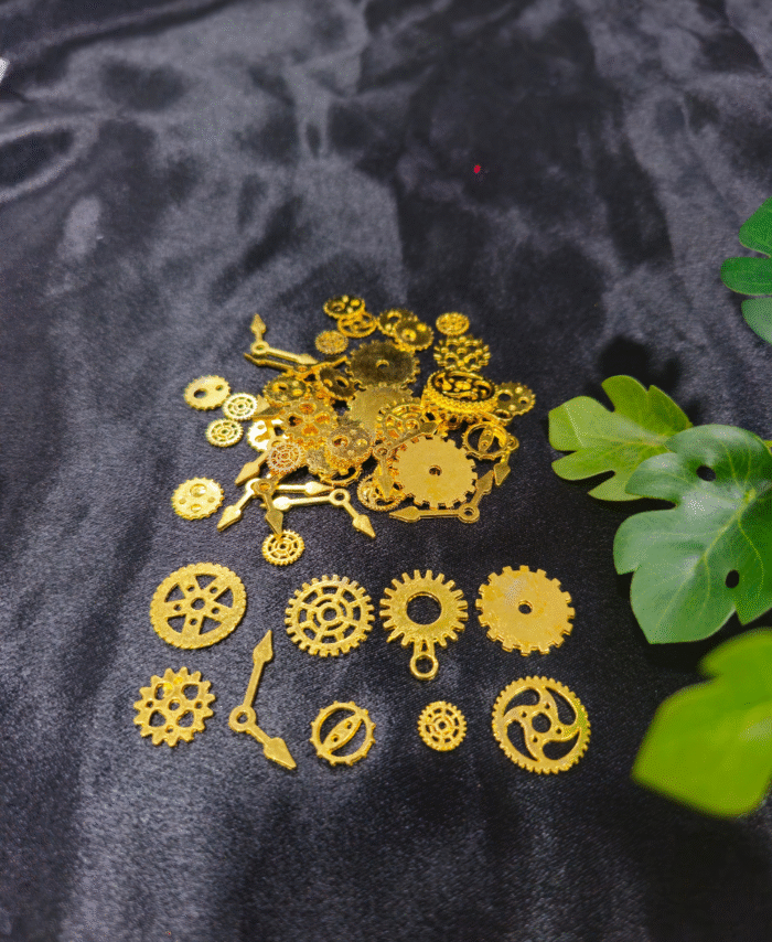 Golden steampunk gears and clock parts scattered on a black background for resin craft use. Various gold metal gears, cogs, and clock hands are displayed for DIY resin jewellery making.