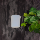 Transparent plastic measuring cup placed on dark background with green plant.