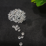 Clear faceted crystals are scattered on black fabric, with a green leaf visible in the corner.