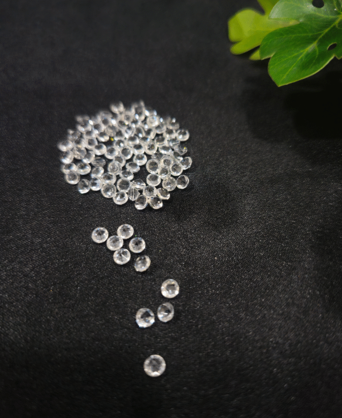 Clear faceted crystals are scattered on black fabric, with a green leaf visible in the corner.