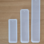 Three transparent silicone bookmark moulds in small, medium, and large sizes on a wooden surface 3-in-1 bookmark mould set with hole for tassels