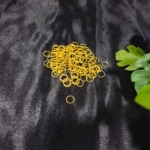 Gold metal jump rings arranged on a black fabric background with green leaves.
