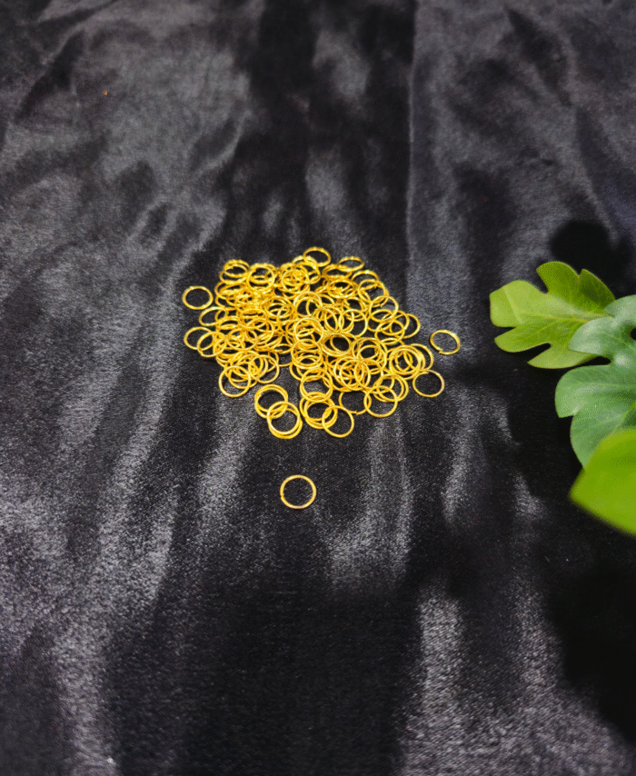 Gold metal jump rings arranged on a black fabric background with green leaves.