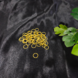 Gold metal jump rings arranged on a black fabric background with green leaves.