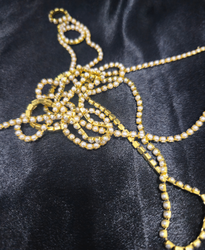 Gold-plated pearl stone chain with small white pearls displayed on black fabric.
