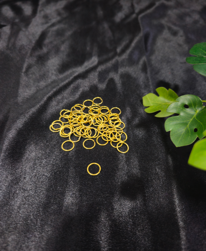 Gold metal jump rings arranged on a black fabric background with green leaves.