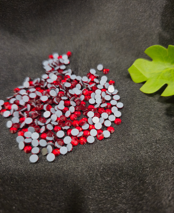 Red flatback rhinestones are scattered on fabric backgrounds with green leaves nearby.