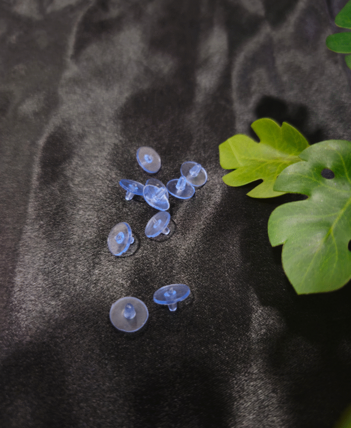 Blue plastic earring stoppers are placed on black fabric with green leaves.