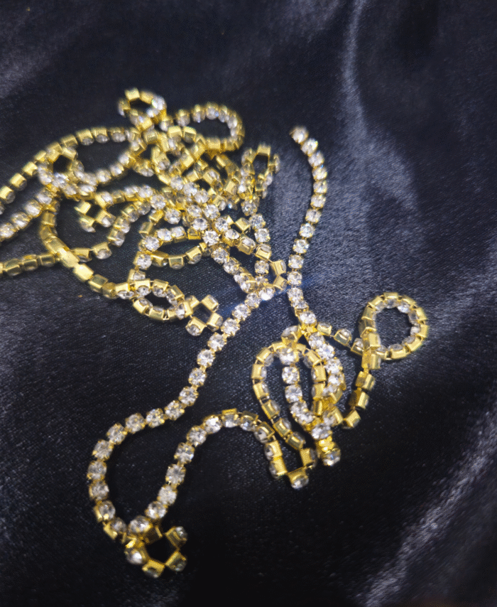 Gold-plated rhinestone chain with clear sparkling stones on black fabric.