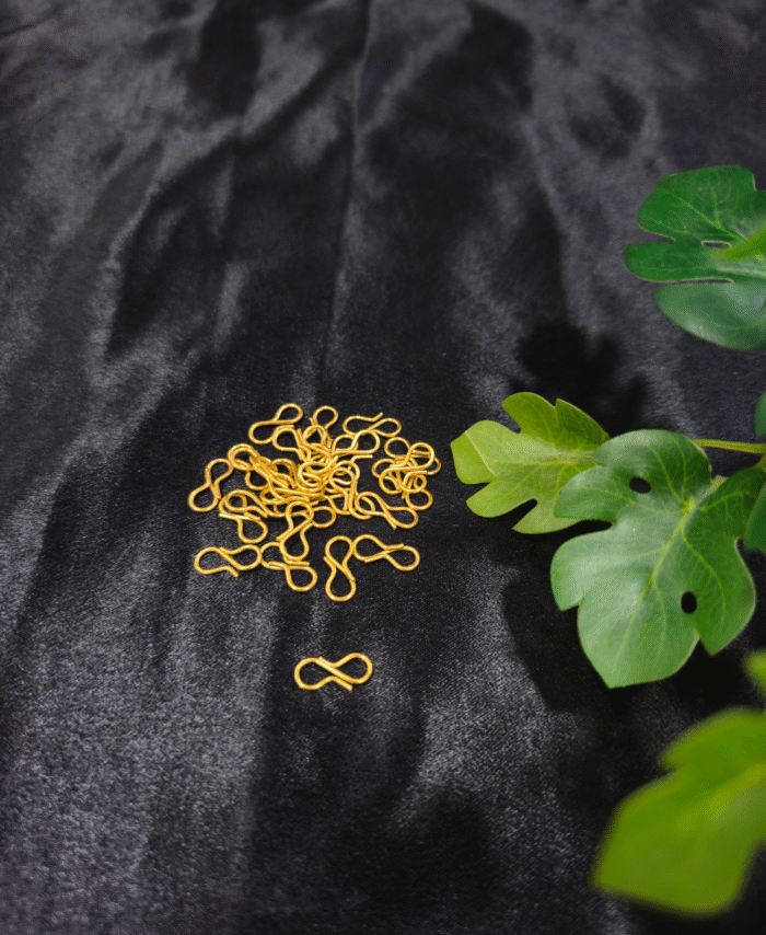 Infinity-shaped metal jewellery connector hooks in gold placed on a black background