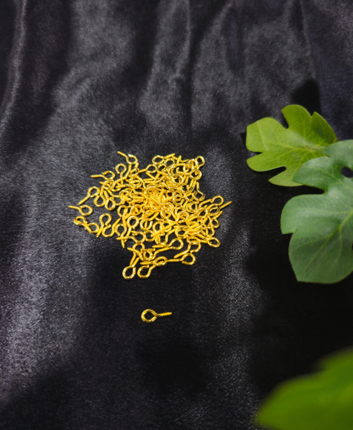 Big Gold Q Hook screws placed on a black textured surface with green leaves beside them.