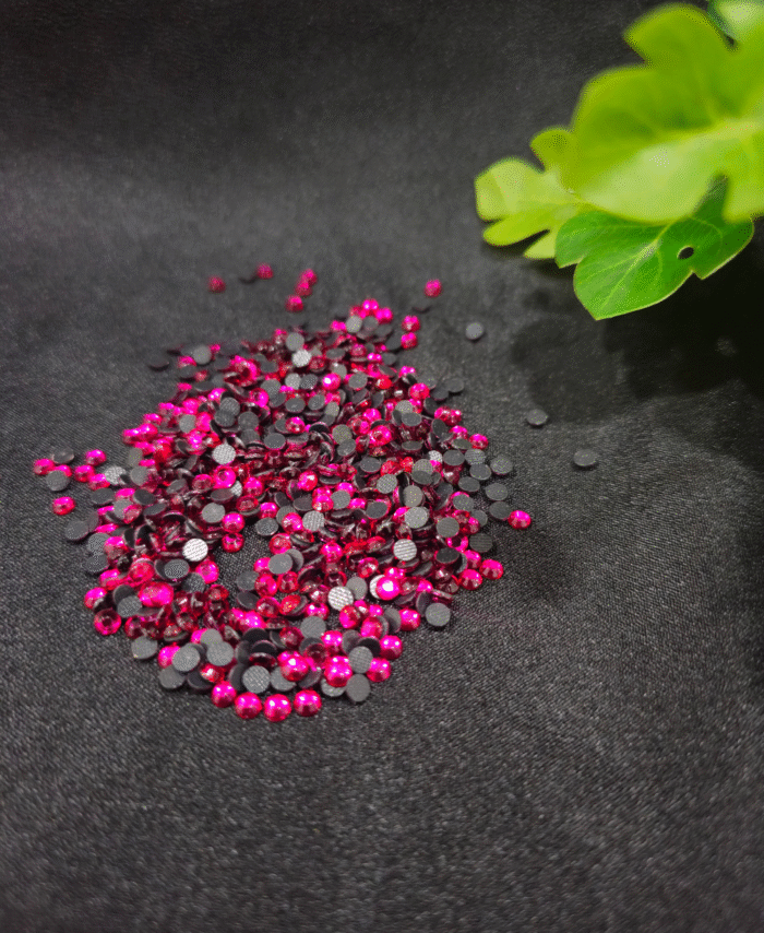 Pink flatback rhinestones are scattered on fabric backgrounds with green leaves nearby.