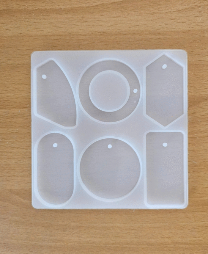 Clear silicone mould with six bag tag shapes placed on a wooden surface.