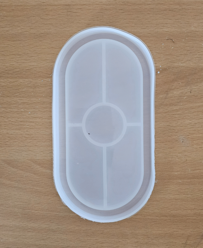 Translucent oval silicone mold with five compartments—central circle and four rectangles—on wood surface.
