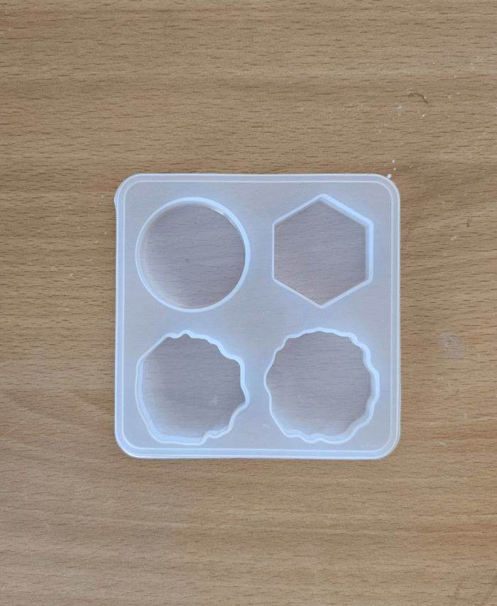 White plastic tray with four 1-inch circular cavities for crafting pop sockets shaped , placed on a wooden surface.