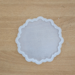 agate-style coaster with scalloped edges and embossed mandala design, placed on wood.