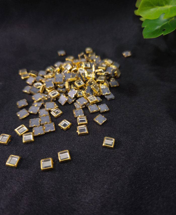 Golden crystal flatback studs are scattered on black velvet fabric with greenery in the corner.