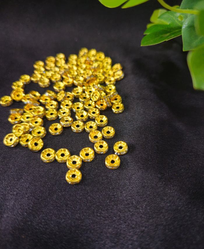 Pile of glossy golden spacer beads displayed on dark fabric with decorative leaves