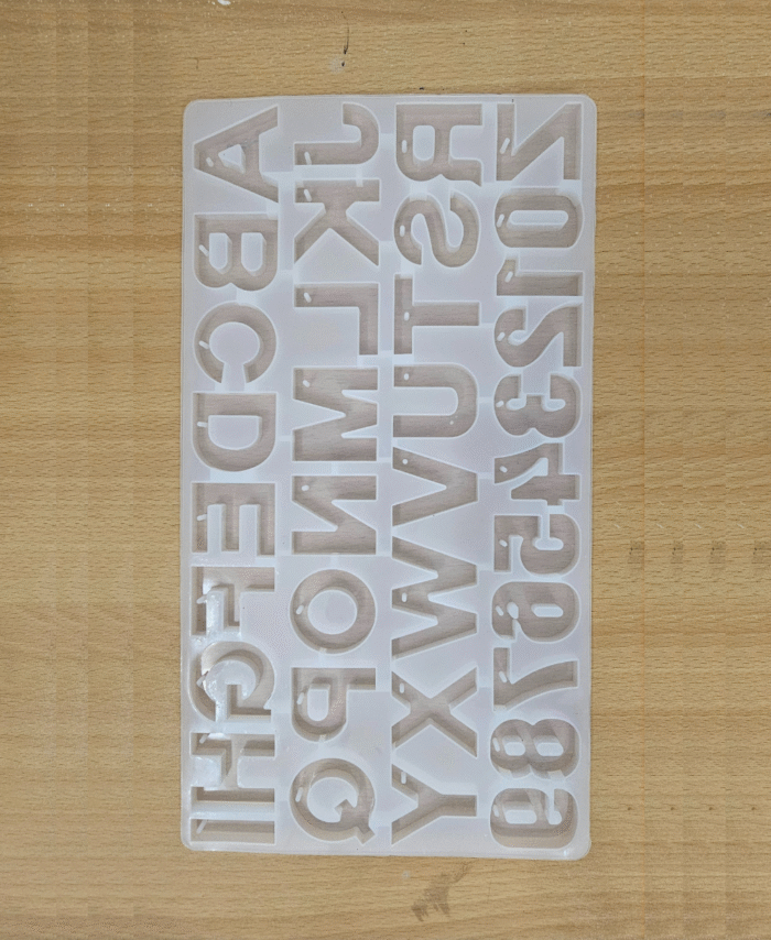 Transparent silicone alphabet mould containing A–Z letters with keychain holes placed on a wooden surface