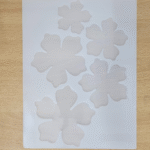 “Silicone mould with five flower-shaped cavities in multiple sizes placed on a wooden background.”