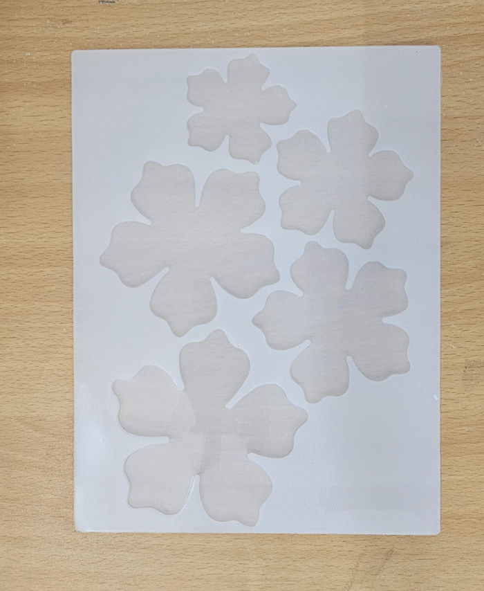 “Silicone mould with five flower-shaped cavities in multiple sizes placed on a wooden background.”
