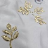 Gold metal leaf branch charm with detailed textured leaves placed on a white background.