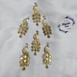 Decorative gold peacock metal charms arranged on a white fabric background.