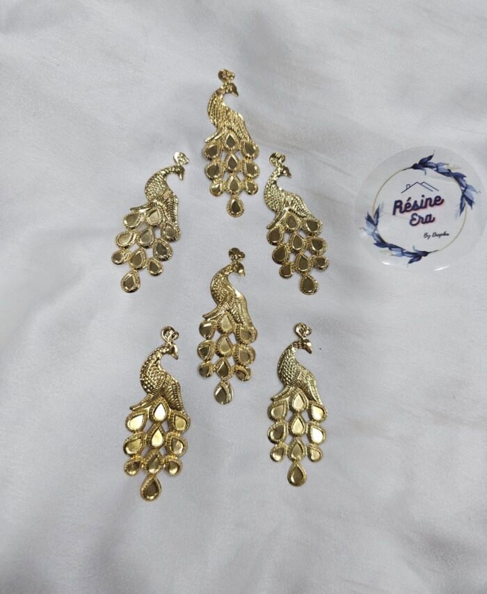 Decorative gold peacock metal charms arranged on a white fabric background.