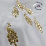 Decorative gold peacock metal charms arranged on a white fabric background.
