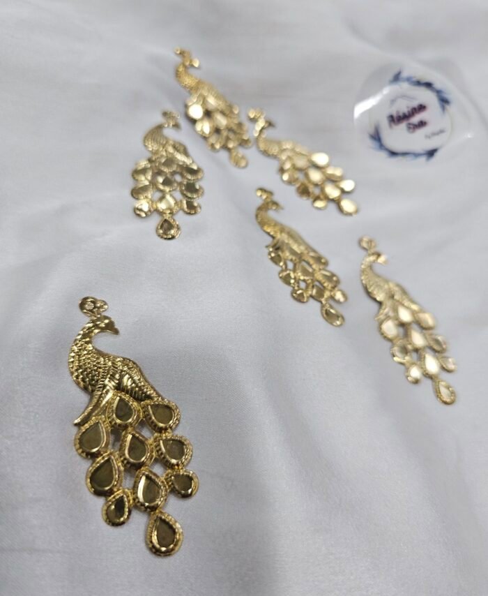 Decorative gold peacock metal charms arranged on a white fabric background.