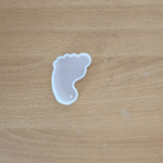 “Small transparent silicone mould in a baby footprint shape placed on a wooden surface.”