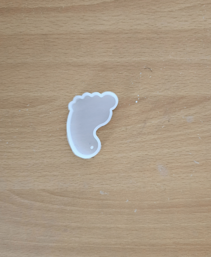 “Small transparent silicone mould in a baby footprint shape placed on a wooden surface.”
