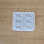 Oval silicone mould with six cavities for making resin rakhis, placed on a wooden surface.