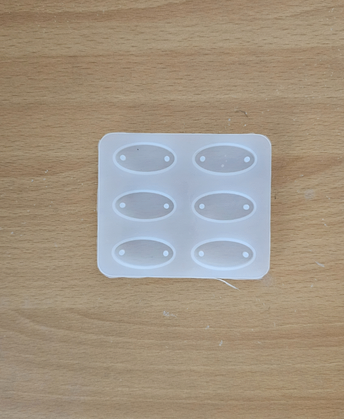 Oval silicone mould with six cavities for making resin rakhis, placed on a wooden surface.