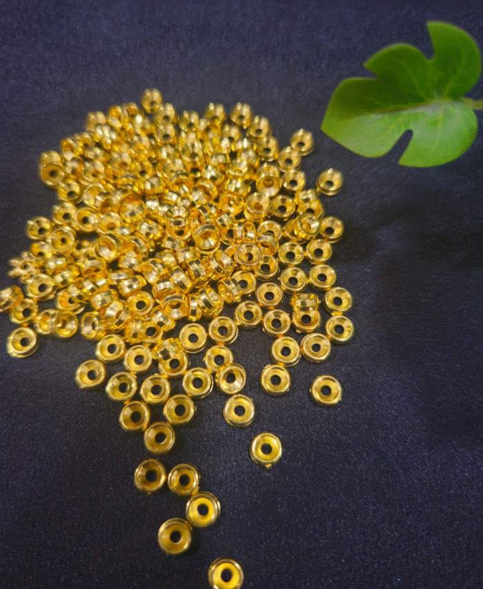 Golden round spacer beads arranged on a black fabric background with green leaf decor