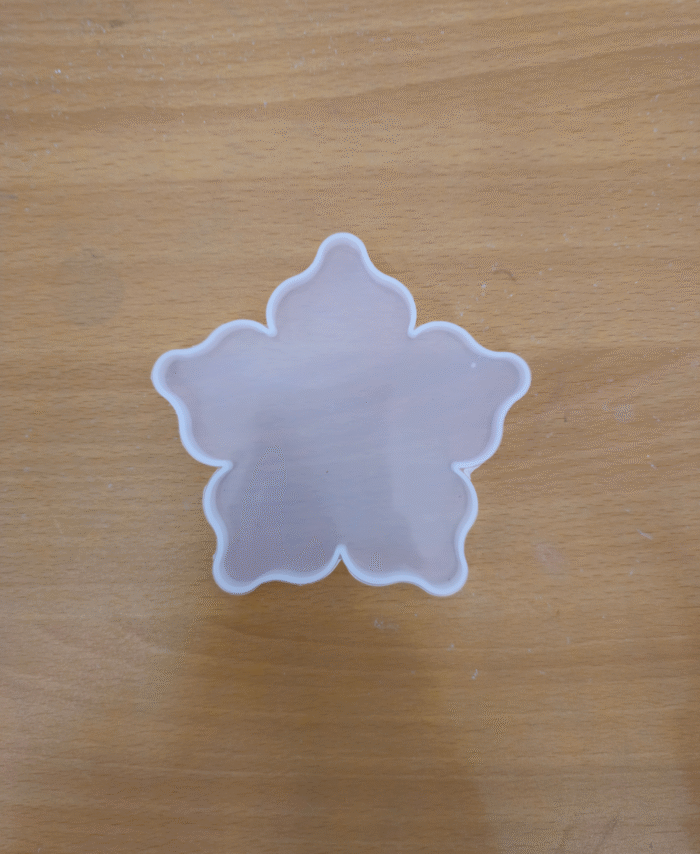 Flower-shaped silicone resin mould with five rounded petals placed on a wooden surface