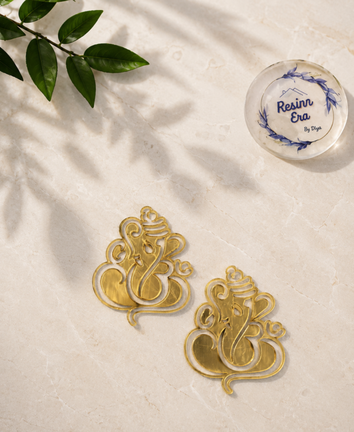 crylic Ganesh motifs with intricate detailing are placed on white satin fabric.