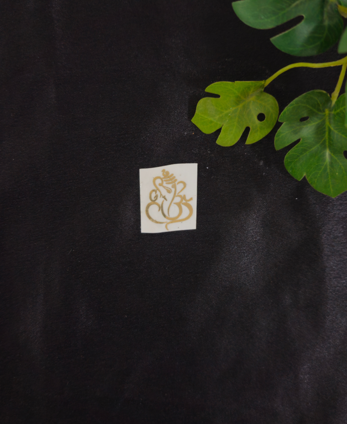 Small golden sticker placed on a black background with green leaves in the top right corner.