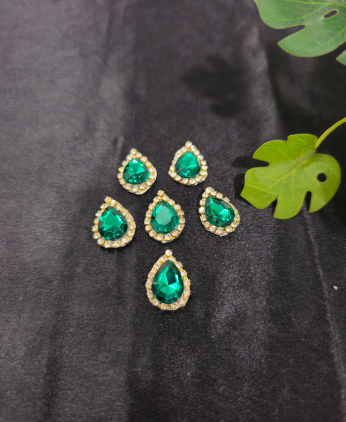 Green teardrop embellishment stones with a diamond border are placed on a black background with green leaves beside them.