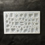 Transparent silicone resin mould with multiple geometric and heart-shaped cavities arranged on a dark fabric background.