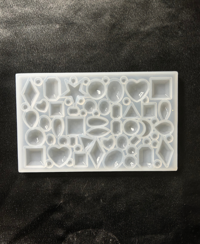 Transparent silicone resin mould with multiple geometric and heart-shaped cavities arranged on a dark fabric background.
