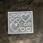 Transparent silicone resin mould with multiple heart shapes in different sizes placed on a dark fabric background.