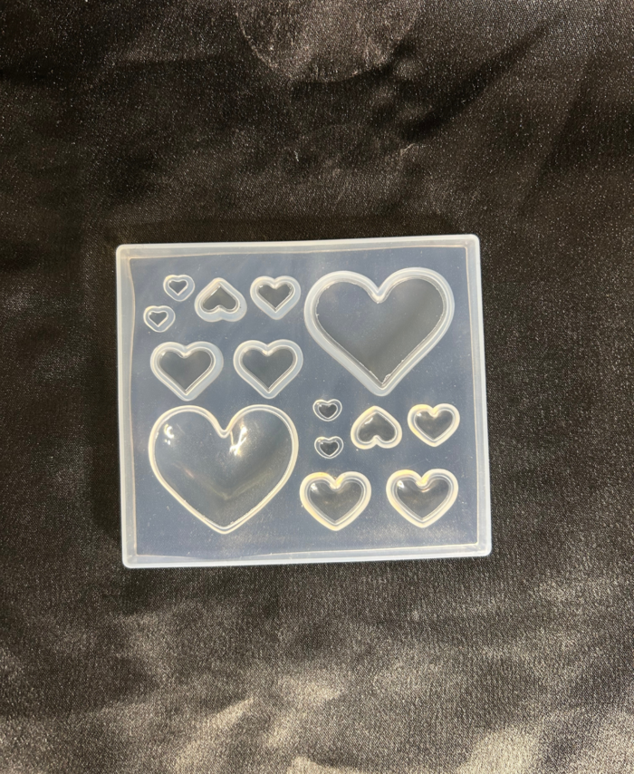Transparent silicone resin mould with multiple heart shapes in different sizes placed on a dark fabric background.