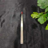 A slim precision tweezer tool is placed on a black background with green leaves beside it.