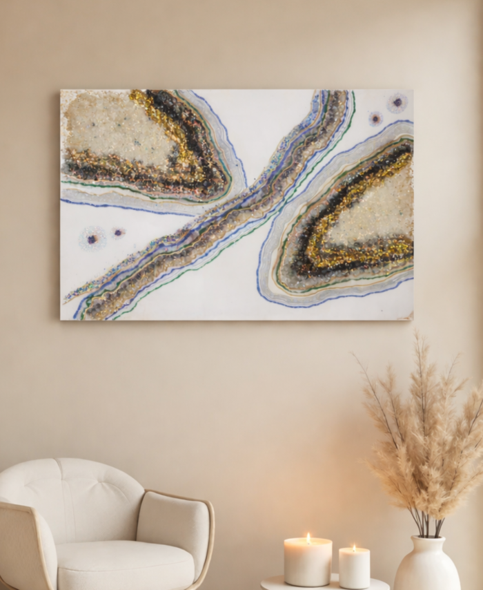 Neutral geode wall art with gold, blue, and green accents displayed on a beige wall above a modern chair and candles