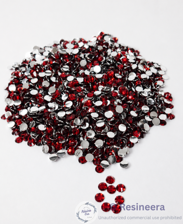 Red flatback rhinestones are scattered on fabric backgrounds with green leaves nearby.